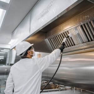 Technician in protective gear pressure washing commercial kitchen hood baffle filters